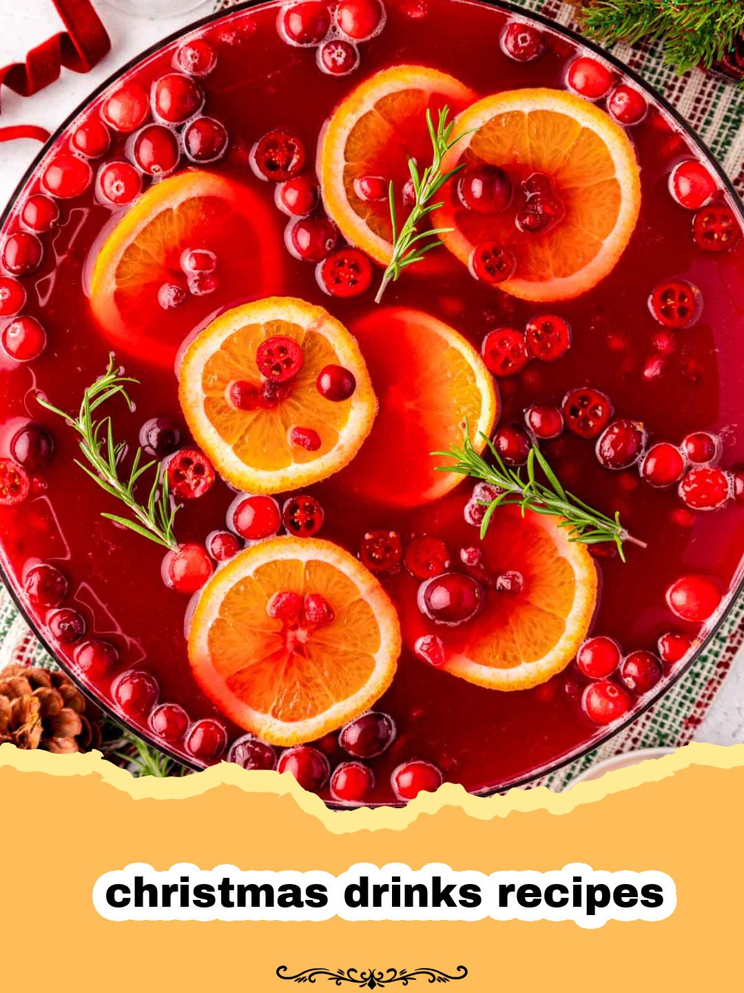 A large glass punch bowl filled with ruby-red Cranberry Pomegranate Punch, garnished with fresh cranberries, rosemary sprigs, and orange slices. Small glass cups are placed around the bowl.