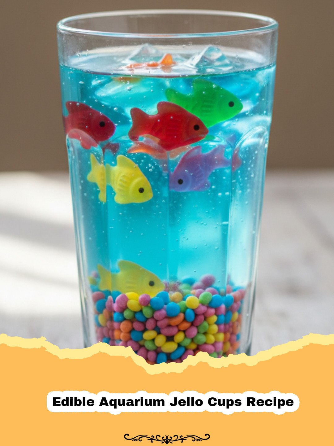 Edible Aquarium Jello Cups Recipe - Close-up of an Edible Aquarium Jello Cup with gummy fish swimming in blue jello over a crushed cookie 'sand' bottom.