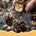 A close-up shot of several Frozen Banana Snickers Bites on a parchment-lined tray, showing the chocolate coating and peanut topping.