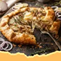 A close-up of a rustic Cheddar, Potato & Caramelized Onion Galette with a golden, flaky crust and visible layers of potatoes, onions, and melted cheddar.